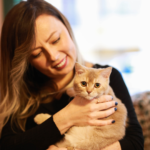 Mujer que sonrie con su gato naranja con ojos naranja